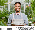 Beautiful confident waiter barista butler man holding tray with glasses in hand, stylish clothes and apron, working in trendy loft style cafe. Restaurant worker concept. 135800369