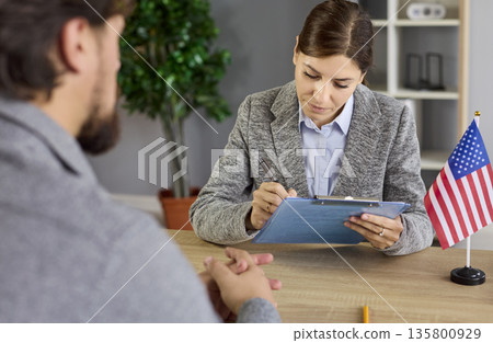 Visa interview at US embassy office with officer reviewing applicant documents 135800929