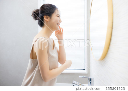 Young woman looking in the mirror in the bathroom 135801323