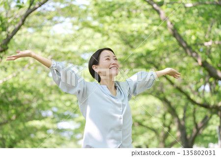 A woman in her 40s taking a deep breath outdoors A woman in her 40s taking a deep breath outdoors 135802031