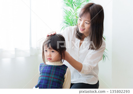 Mother tying girl's hair 135802293