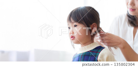 Mother tying girl's hair 135802304
