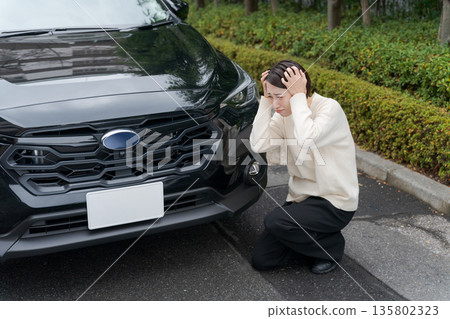 A woman crouches on the road after crashing her car 135802323