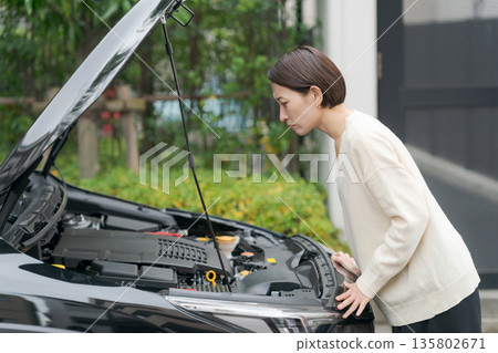 A woman opens the hood of her car after it breaks down 135802671