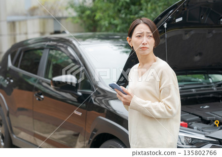 一位汽車拋錨的女士透過電話聯繫了某人。 一位汽車拋錨的女士透過電話聯繫了某人。 135802766