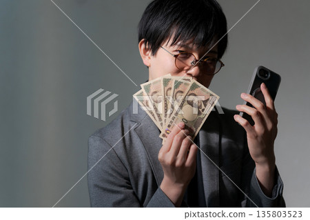 可疑男子手持智慧型手機和現金 135803523