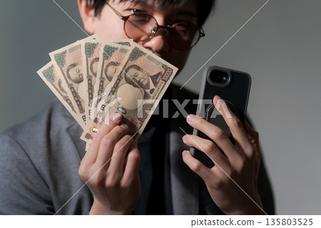 Suspicious man holding smartphone and money Suspicious man holding smartphone and money 135803525