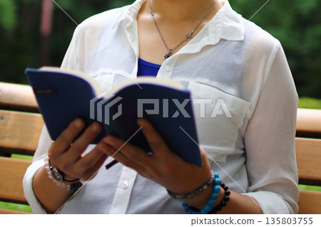 A woman reading a book on the bench 135803755