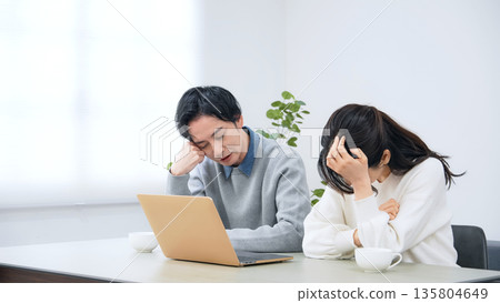 A depressed couple looking at a laptop in their room 135804649