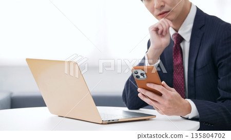 Male business person using laptop and smartphone in office 135804702