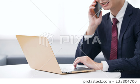 Male business person using laptop and smartphone in office 135804706
