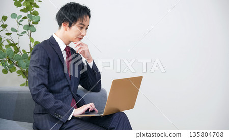 Male business person thinking while looking at a laptop in the office 135804708