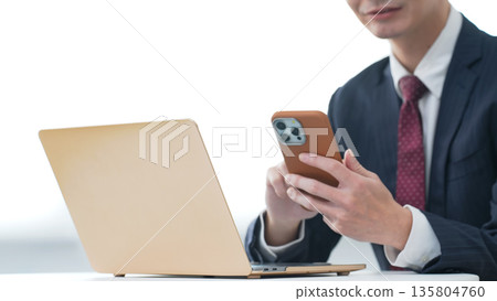 Male business person using laptop and smartphone in office 135804760