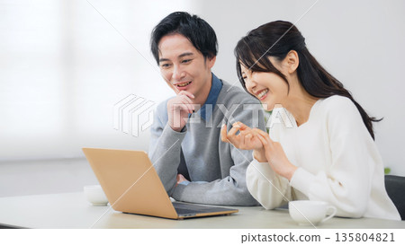 A couple looking at a laptop in a room A couple looking at a laptop in a room 135804821