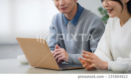 A couple looking at a laptop in a room A couple looking at a laptop in a room 135804822