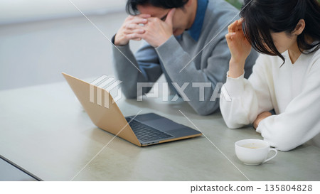 一對情緒低落的夫婦在房間裡看著筆記型電腦。 一對情緒低落的夫婦在房間裡看著筆記型電腦。 135804828