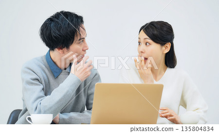 A surprised couple looking at a laptop in a room A surprised couple looking at a laptop in a room 135804834