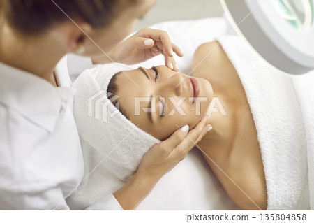 Woman cosmetologist exam young woman skin condition under lamp in beauty spa salon. 135804858