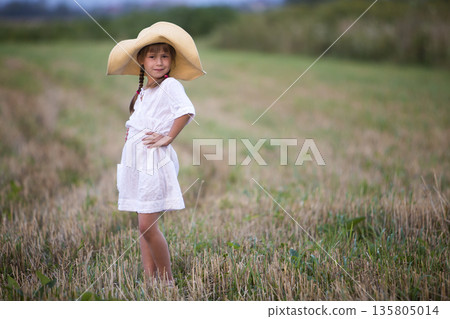 Young fashionable lovely cute girl with long braids in nice white summer dress and big straw hat. 135805014