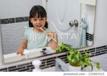 girl child brushing teeth at reflection in mirror in bathroom girl child brushing teeth at reflection in mirror in bathroom 135805525