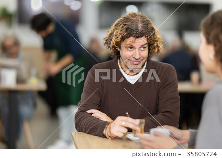 Happy middle-age man and young girl chatting over cup of coffee at table in light cafe, face of middle-age man and back of girl Happy middle-age man and young girl chatting over cup of coffee at table in light cafe, face of middle-age man and back of girl 135805724