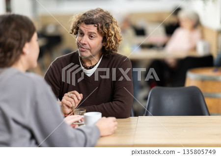 Positive man in cafe sits near female companion, has nice conversation and discusses news of day Positive man in cafe sits near female companion, has nice conversation and discusses news of day 135805749