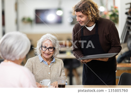 Male waiter brings order to elderly women Male waiter brings order to elderly women 135805760