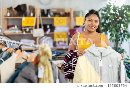 Happy young girl choosing down jacket in clothing store 135805764