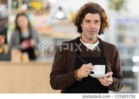 Working days in bakery, man worker of mini bakery prepares to meet cafe visitors. Working days in bakery, man worker of mini bakery prepares to meet cafe visitors. 135805792