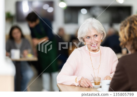 Older woman sitting at a table in a coffee shop and listening to a man Older woman sitting at a table in a coffee shop and listening to a man 135805799