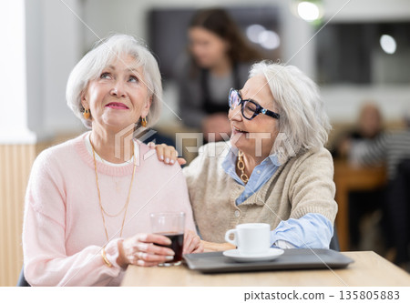 Two senior women colleagues meeting and drinking coffee at table in cafeteria 135805883