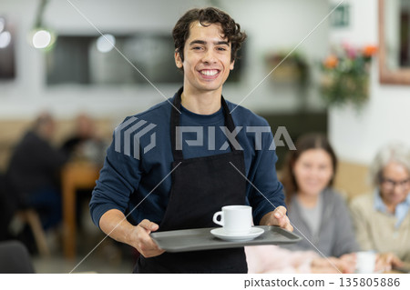 Working days in bakery, guy worker of mini bakery prepares to meet cafe visitors. Working days in bakery, guy worker of mini bakery prepares to meet cafe visitors. 135805886