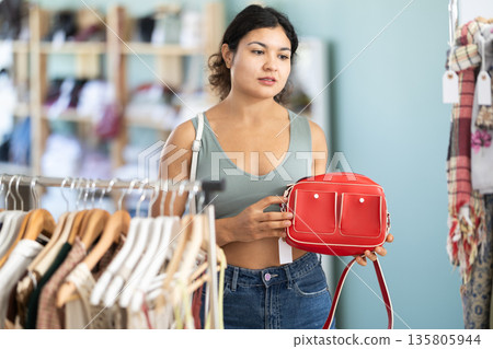 Latina woman choosing a stylish handbag in store with interest 135805944