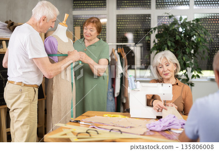 Aged woman stitching at machine during sewing class for seniors 135806008