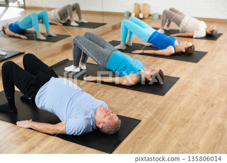 People of different ages performing glute bridge during group Pilates workout. Active lifestyle and wellness concept 135806014