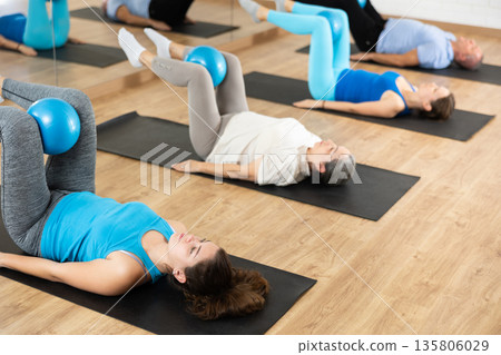 Group of young elderly people in sportswear exercising Pilates with mini balls while lying on mats in rehabilitation center 135806029