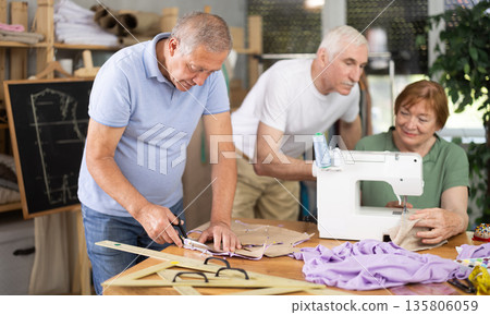 Elderly participants in sewing coterie learn sewing, communicate and talking, sewing, cut fabric by scissors Elderly participants in sewing coterie learn sewing, communicate and talking, sewing, cut fabric by scissors 135806059