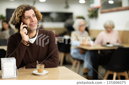 Handsome middle-aged man drinking fresh coffee at table in cafe and talking at mobile phone Handsome middle-aged man drinking fresh coffee at table in cafe and talking at mobile phone 135806075