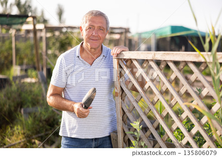 Portrait of happy elderly man with hoe in her hands in her garden Portrait of happy elderly man with hoe in her hands in her garden 135806079