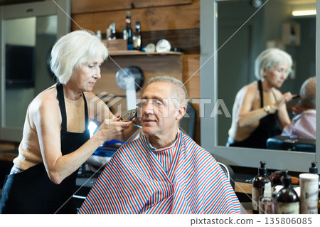 Experienced mature woman master makes performs haircut for elderly man with clipper Experienced mature woman master makes performs haircut for elderly man with clipper 135806085