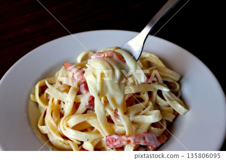 Tagliatelle carbonara lifted with a fork on the table background Tagliatelle carbonara lifted with a fork on the table background 135806095