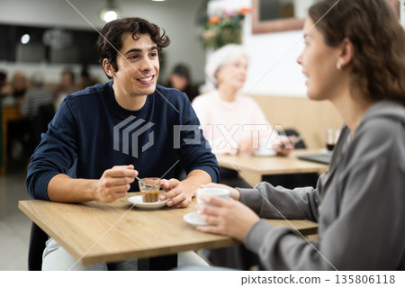 Young couple drinking coffee and chatting while sitting at table in cozy cafe 135806118