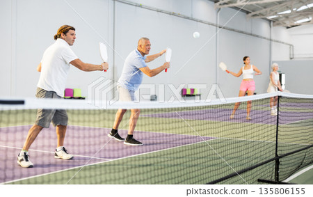 Focused adult man playing pickleball match in team with older partner 135806155