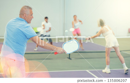 Rear view of elderly man playing pickleball on indoor court 135806207