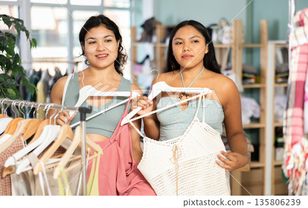 Two young women choosing summer dresses or tops in clothing store Two young women choosing summer dresses or tops in clothing store 135806239