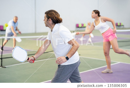 Sporty man pickleball tennis player trains on the indoor court using a racket to hit ball Sporty man pickleball tennis player trains on the indoor court using a racket to hit ball 135806305