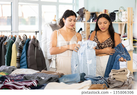Two girlfriends chooses fashionable jeans in fashionable clothing store Two girlfriends chooses fashionable jeans in fashionable clothing store 135806306