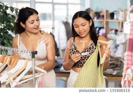 Two girlfriends chooses dresses or o tops for the summer period in fashionable clothing store Two girlfriends chooses dresses or o tops for the summer period in fashionable clothing store 135806318