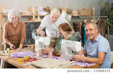 Elderly male showed group of elderly people how to sew on machine Elderly male showed group of elderly people how to sew on machine 135806355