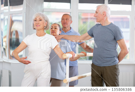 Diligent mature men and women practicing basic positions with trainer standing by ballet 135806386